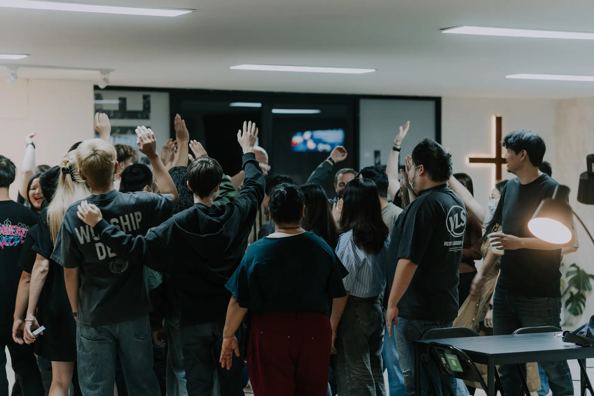 Church members raise their hands in worship before a cross