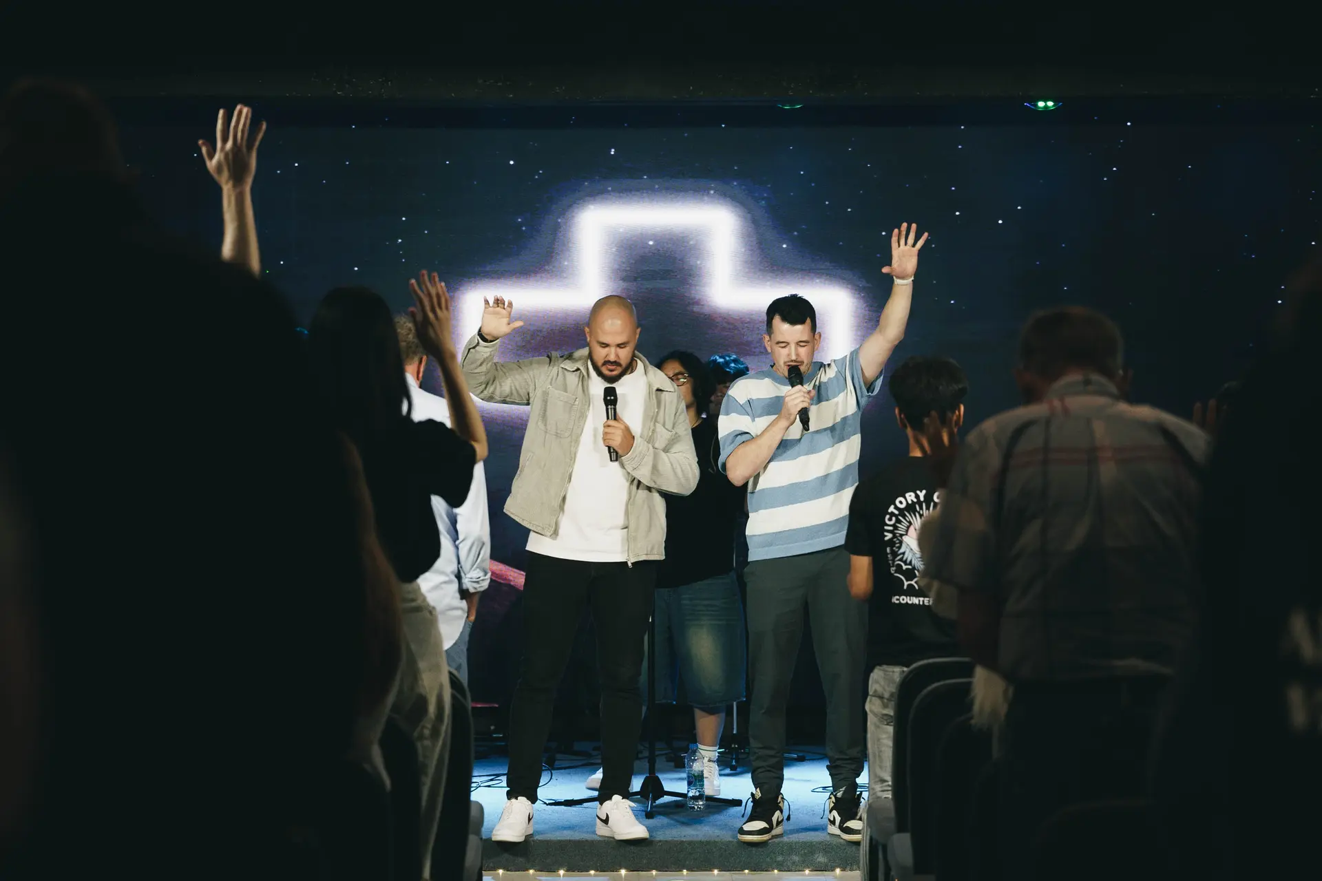 Two men lead worship on stage as the congregation raises their hands
